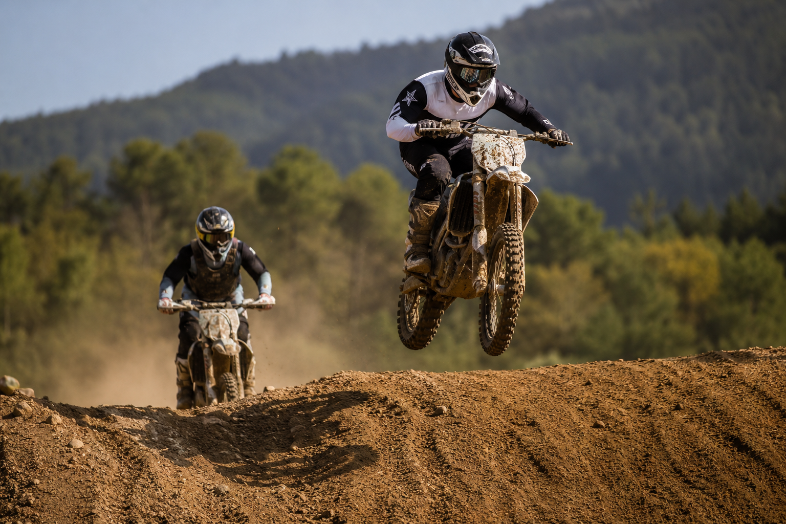 Two motocross riders racing over a dirt jump.